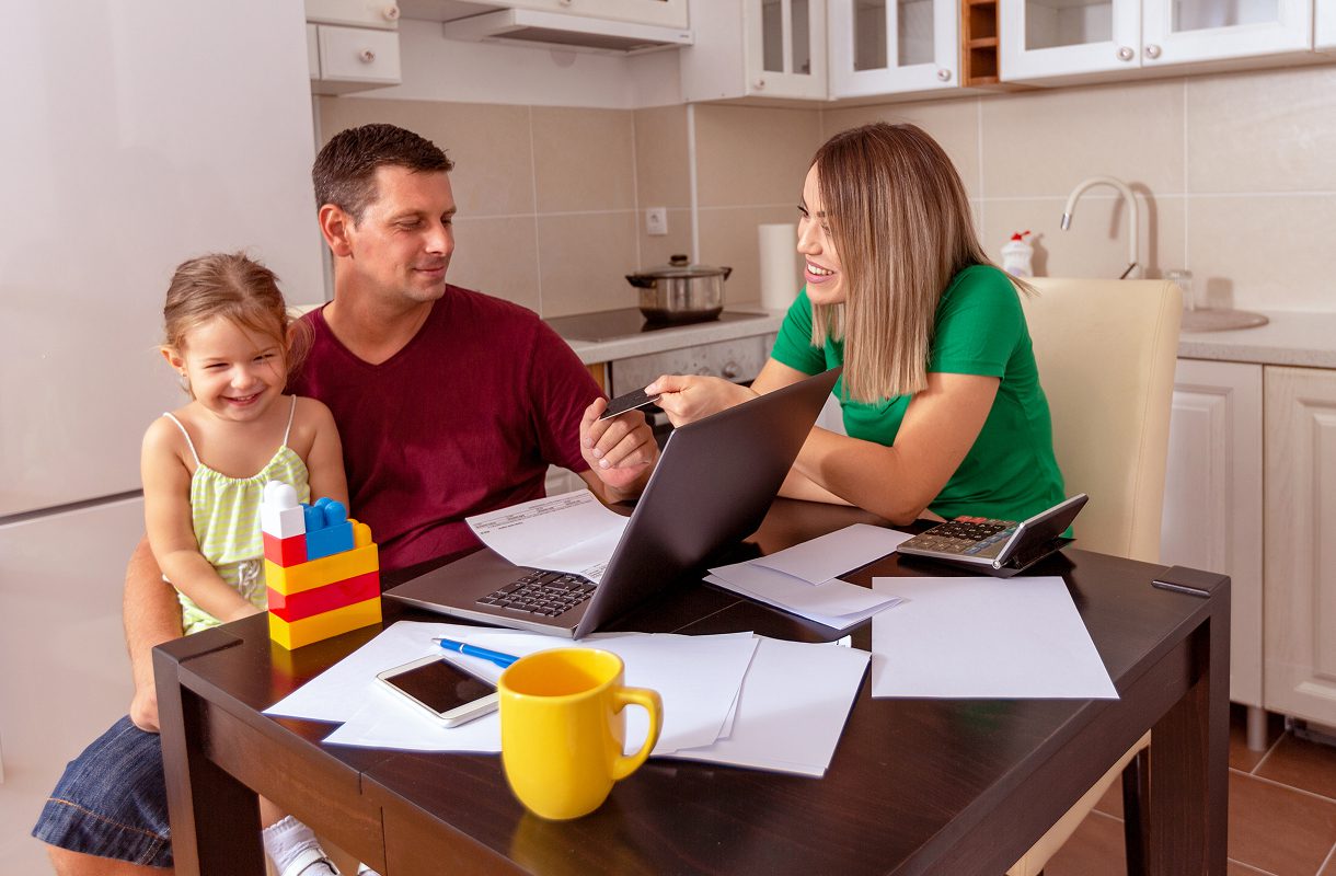Family at table with laptop and papers.